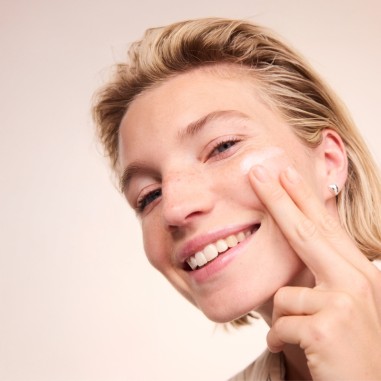 Mujer aplicando la leche limpiadora Basis Sensitive Aloe y Karité de Lavera sobre la piel del rostro.